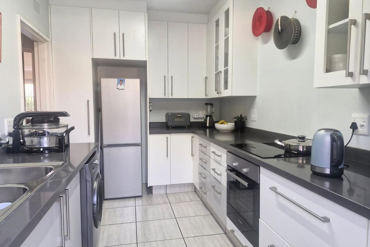 A functional kitchen featuring white cabinetry, dark stone countertops, integrated oven and cooktop, and tiled flooring with a dedicated laundry appliance space.