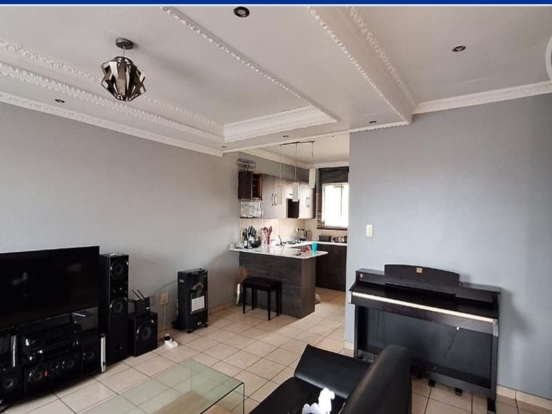 Open-plan living area featuring tiled flooring, decorative ceiling cornices, and a functional kitchen with a breakfast bar.