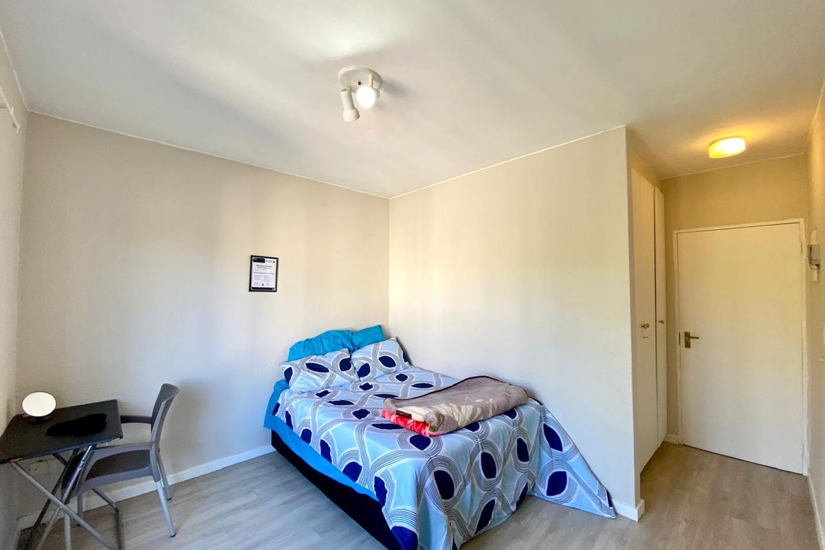 A functional bedroom featuring light-toned laminate flooring, built-in cupboard storage, and neutral wall finishes.