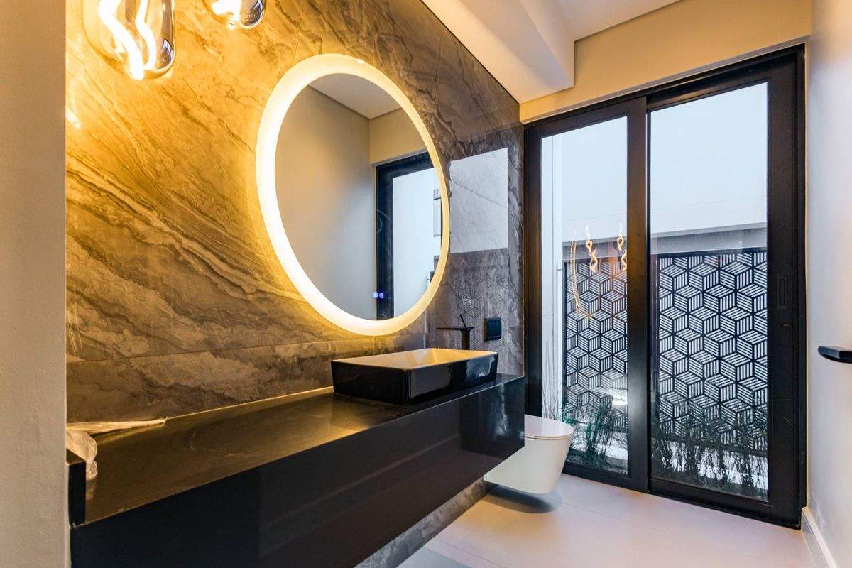 Modern bathroom featuring a floating vanity, vessel sink, backlit circular mirror, and large-format marble-effect wall tiles with floor-to-ceiling glass doors.