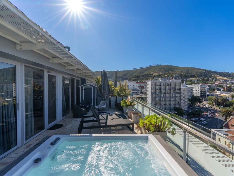 Spacious penthouse balcony featuring a built-in jacuzzi, glass balustrade, and panoramic city and mountain views.