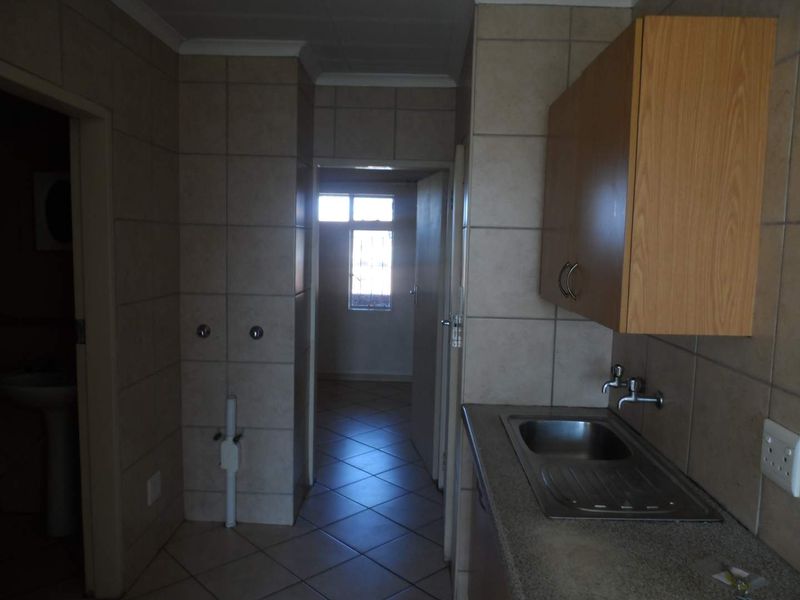 A functional kitchen area featuring tiled walls, built-in cabinetry, and a stainless steel sink, with direct access to adjacent rooms.