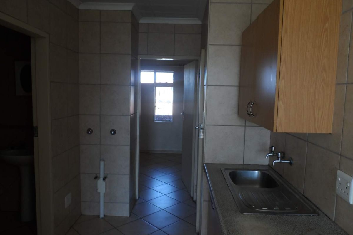 A functional kitchen area featuring tiled walls, built-in cabinetry, and a stainless steel sink, with direct access to adjacent rooms.