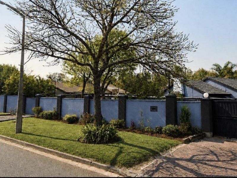 Street view of the property featuring a blue perimeter wall, paved driveway, and secure sliding gate entrance.