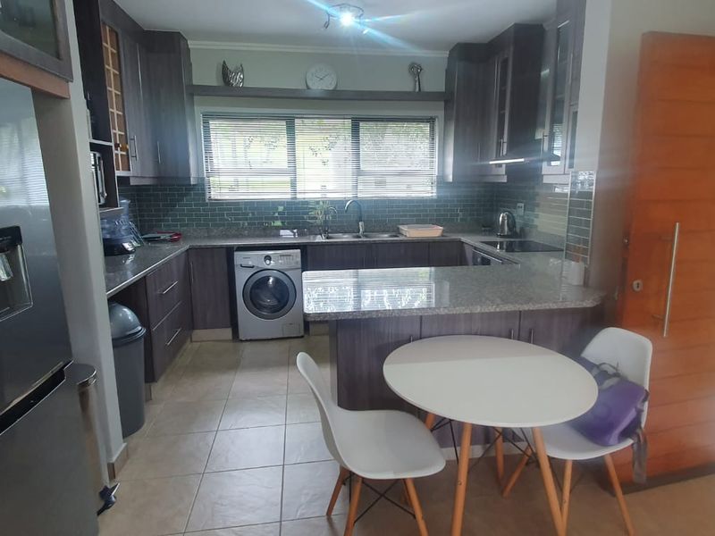 A functional kitchen featuring granite countertops, dark wood cabinetry, a subway tile backsplash, and integrated appliances including a washing machine and hob.