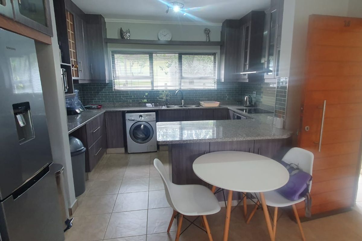 A functional kitchen featuring granite countertops, dark wood cabinetry, a subway tile backsplash, and integrated appliances including a washing machine and hob.