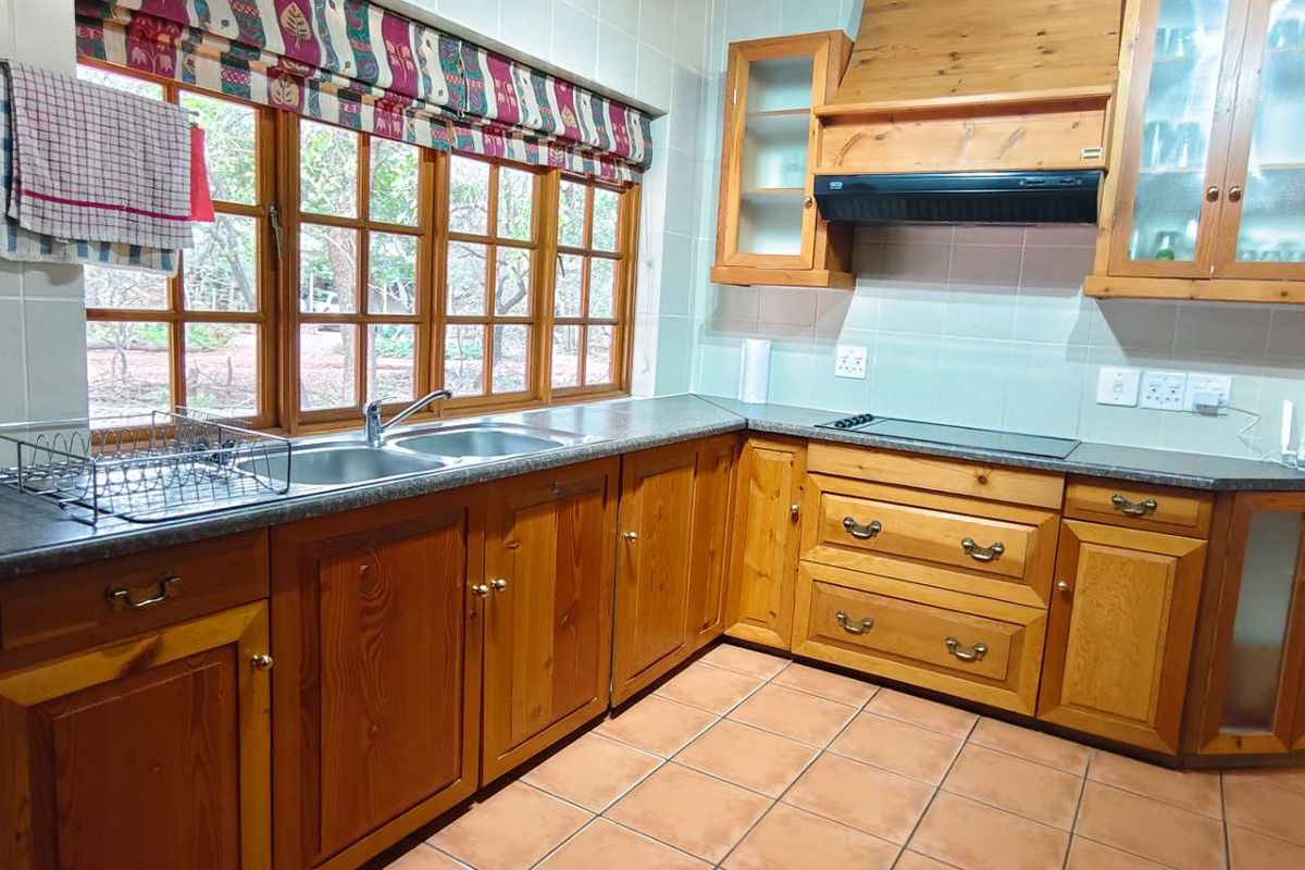 A functional kitchen featuring timber cabinetry, laminate countertops, a built-in hob, and an extractor fan, with tiled flooring and large windows.