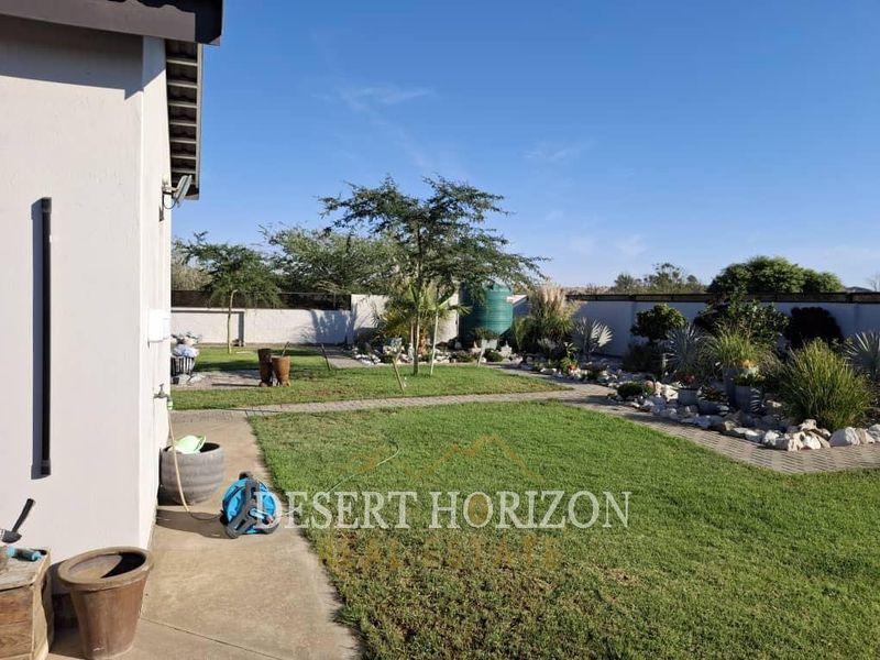 A well-maintained rear garden featuring a lawn, paved pathways, boundary walls, and a water tank, providing a clean and functional outdoor space.