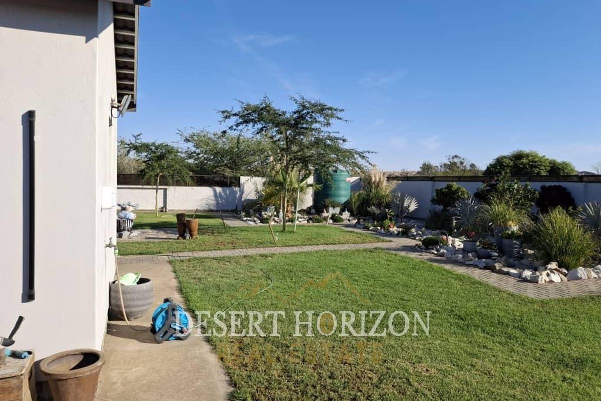A well-maintained rear garden featuring a lawn, paved pathways, boundary walls, and a water tank, providing a clean and functional outdoor space.