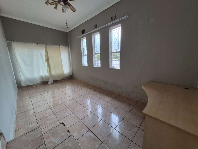An empty living area featuring tiled flooring, a ceiling fan, and a built-in desk, requiring maintenance and cosmetic updates.