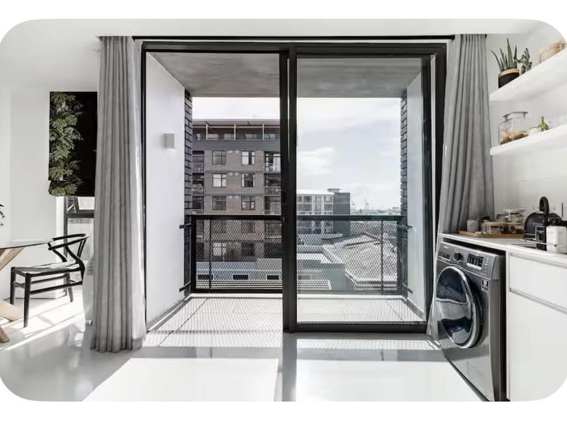 Modern open-plan living area featuring polished concrete floors, built-in shelving, and a seamless transition to a private balcony with urban views.