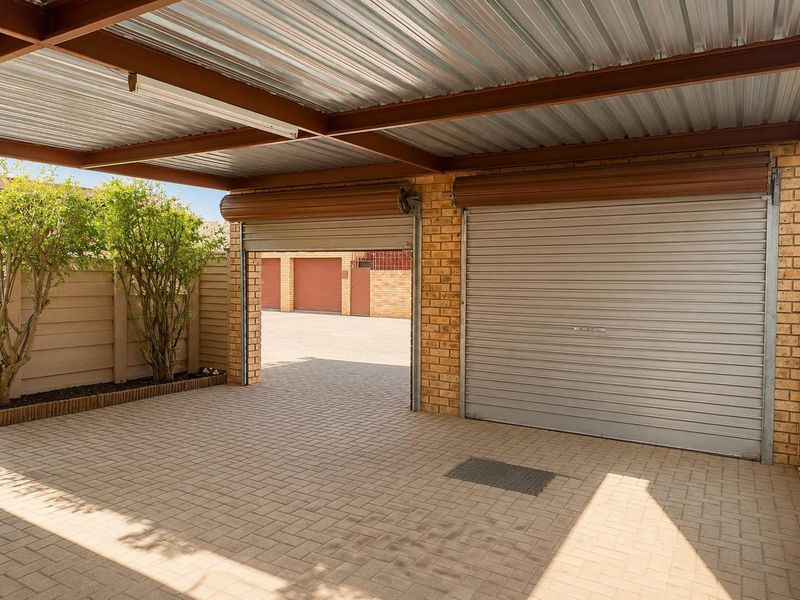 A well-maintained double garage featuring roller doors, a corrugated metal roof, and paved flooring, providing secure parking space.