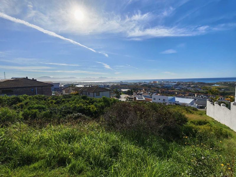A scenic elevated view overlooking a residential neighbourhood with coastal and mountain vistas in the distance.