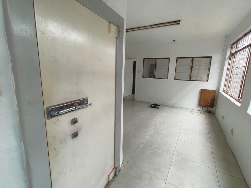 An empty industrial office space featuring tiled flooring, security bars on windows, and a heavy-duty security door.