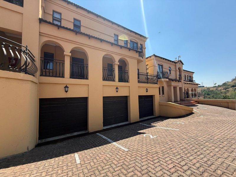 Front elevation of a townhouse complex featuring a triple garage, paved driveway, and upper-level balconies with wrought iron railings.
