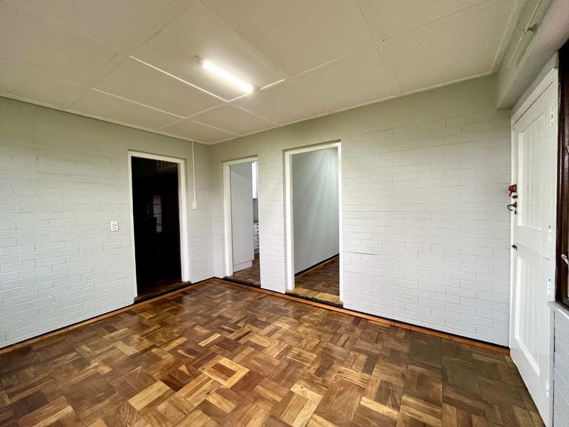 An empty living area featuring classic parquet flooring, painted brick walls, and a neutral ceiling, offering a versatile space ready for personalization.
