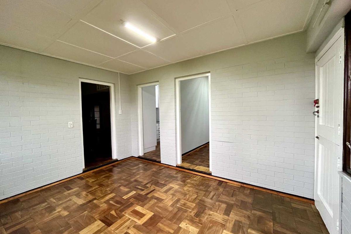 An empty living area featuring classic parquet flooring, painted brick walls, and a neutral ceiling, offering a versatile space ready for personalization.