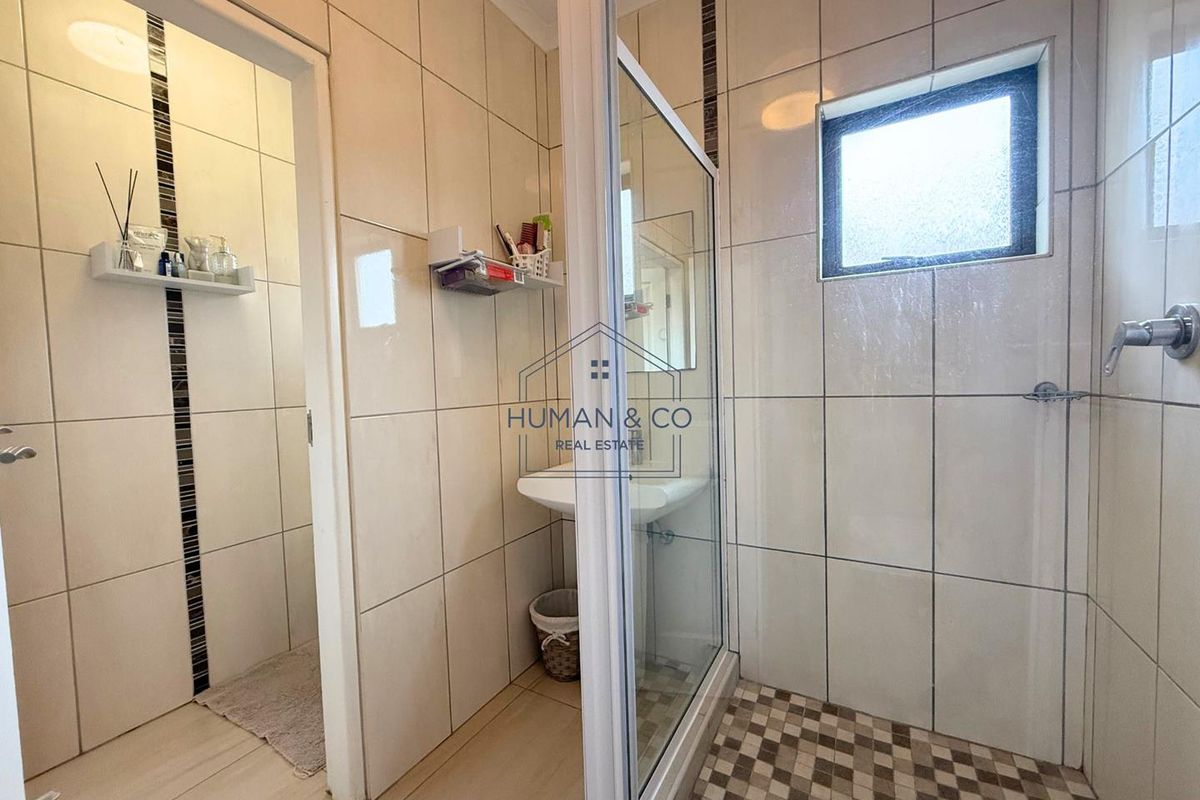 A functional bathroom featuring a glass-enclosed shower with mosaic floor tiles, a pedestal basin, and neutral wall tiling.