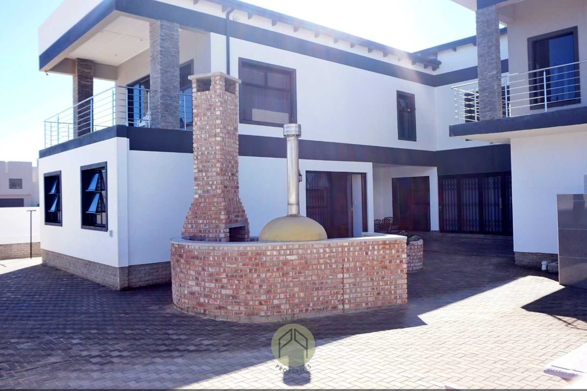 Rear exterior view featuring a paved courtyard, a built-in brick fireplace, and a pizza oven, set against a modern two-story residential building.