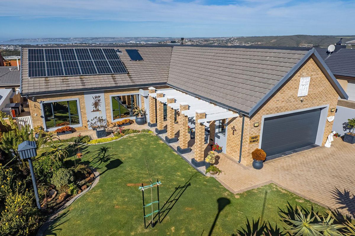 Aerial view of a well-maintained brick house featuring a tiled roof with solar panels, a paved driveway, double garage, and a landscaped front garden.