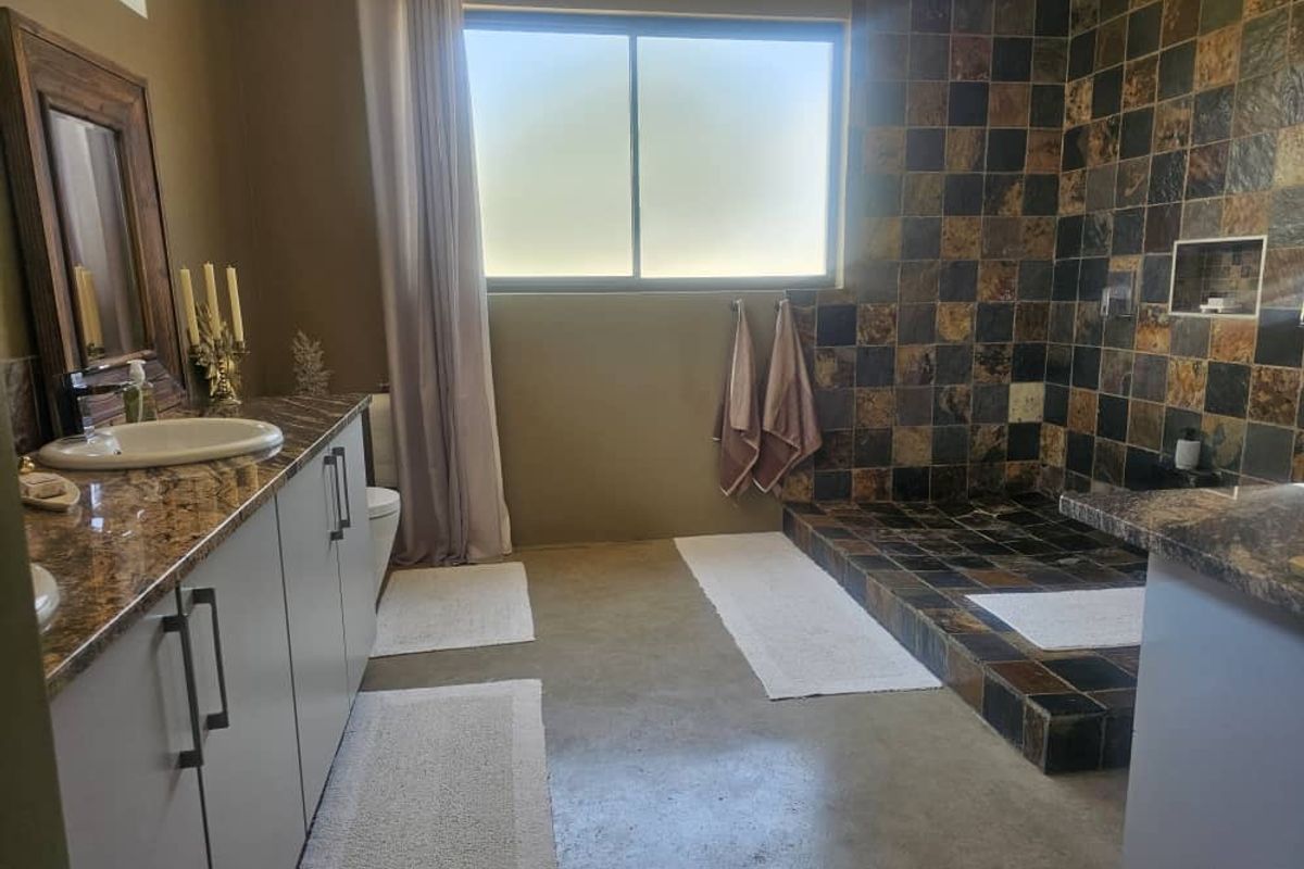 Spacious bathroom featuring a granite-topped vanity, polished concrete floors, and a large walk-in shower with decorative slate tiling.