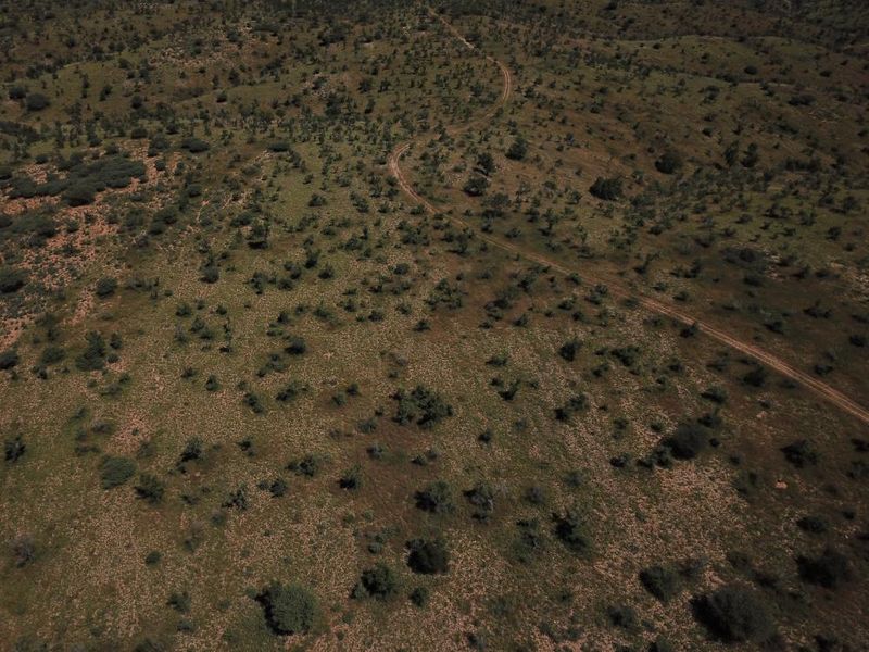An aerial view of a large, undeveloped residential land plot featuring natural vegetation and a dirt access track.