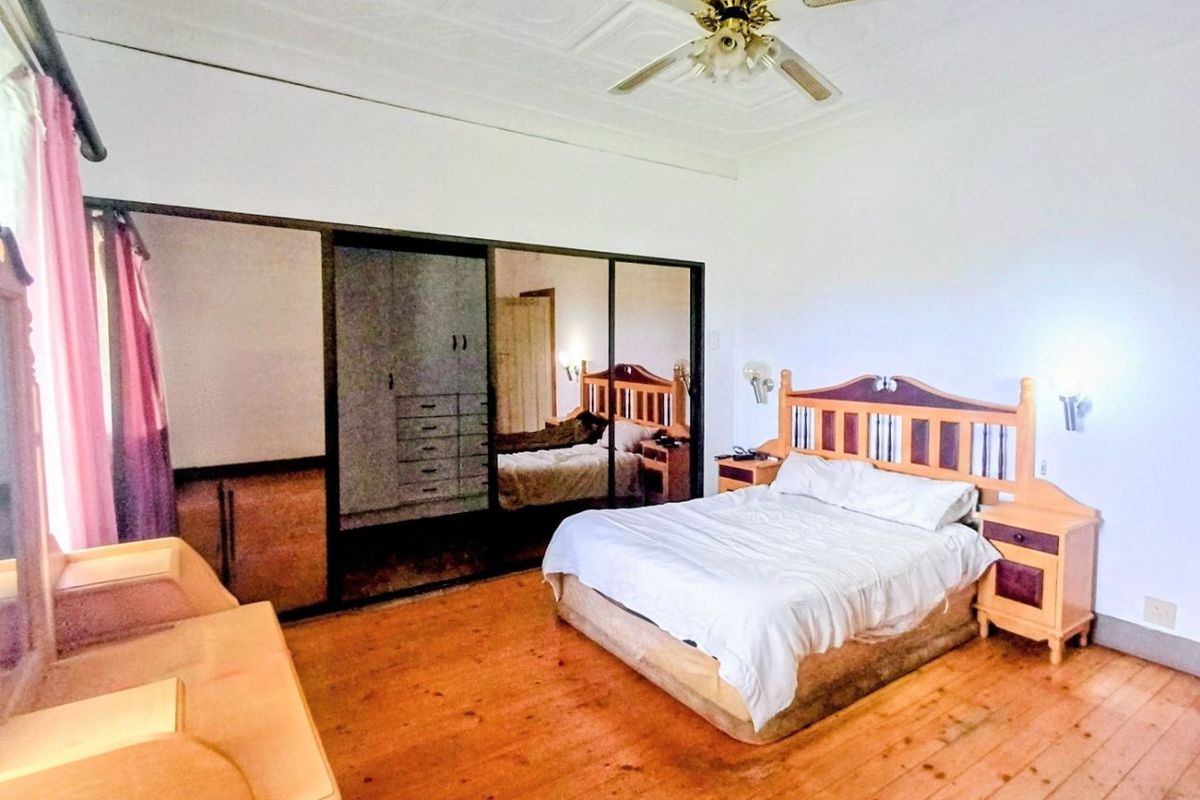 Spacious bedroom featuring original pressed metal ceilings, timber flooring, and large built-in mirrored wardrobes providing ample storage space.