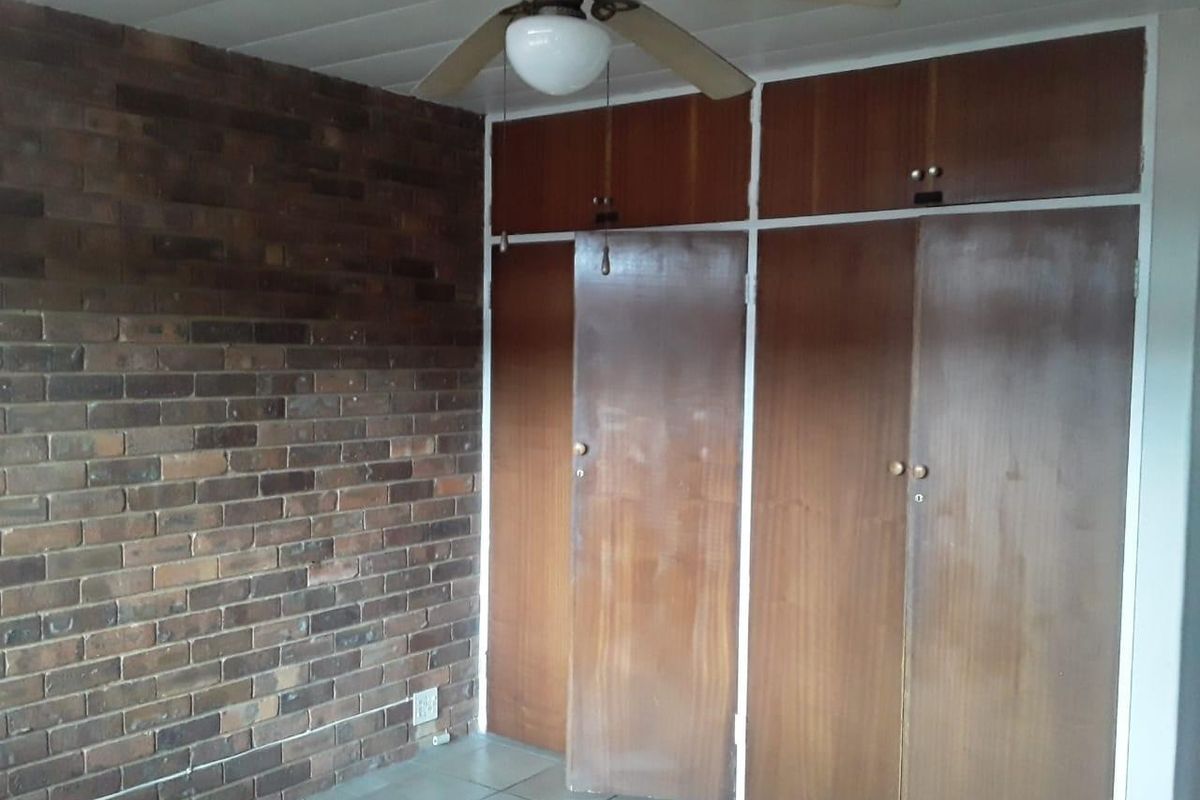 Bedroom featuring a rustic exposed brick feature wall, built-in wooden cupboards with overhead storage, and a ceiling fan.