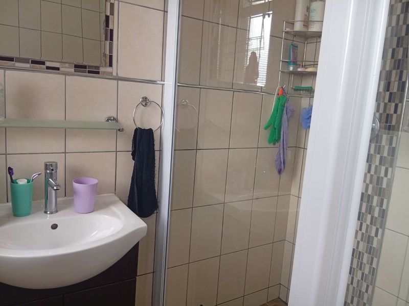 A functional bathroom featuring a vanity basin with mixer tap, a glass-enclosed shower, and neutral wall tiling with a decorative mosaic accent border.
