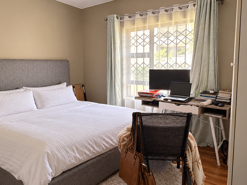 A well-maintained bedroom featuring laminate flooring, a built-in wardrobe, and a window fitted with a security gate.