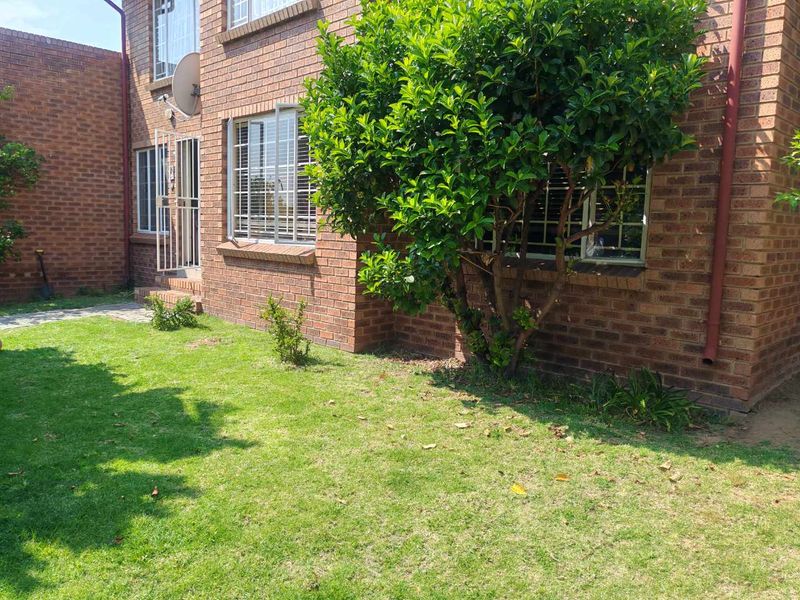 Rear exterior view of a face brick townhouse featuring a small lawn, paved walkway, and security-fitted windows and doors.