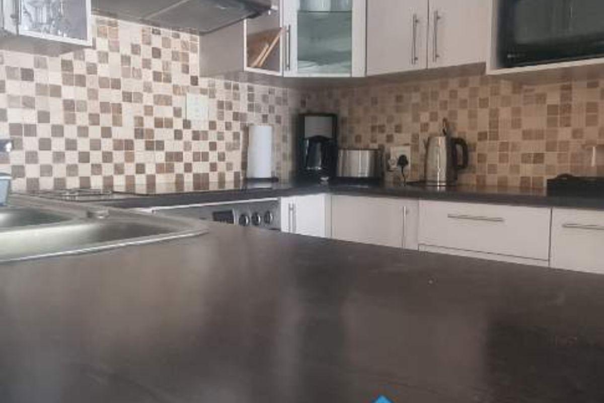 A functional kitchen featuring light-toned cabinetry, a dark countertop, a built-in extractor fan, and a mosaic tile backsplash.
