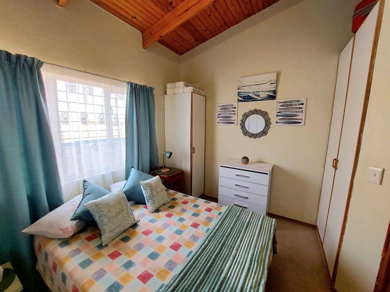 A cozy bedroom featuring exposed timber ceiling beams, built-in wardrobe storage, and security burglar bars on the window.
