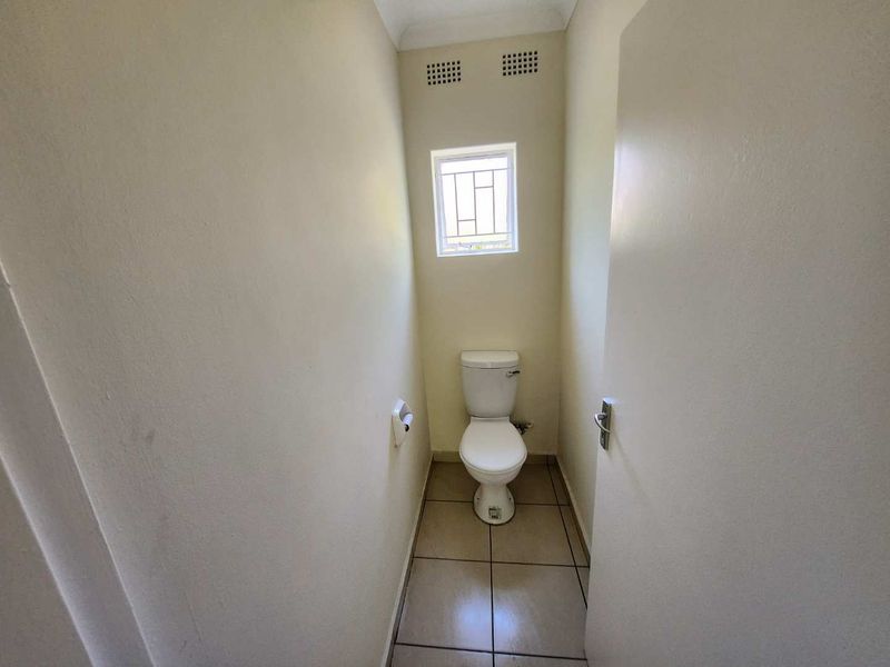 A compact, functional bathroom featuring tiled flooring, a standard toilet, and a small window with a security grille for ventilation.