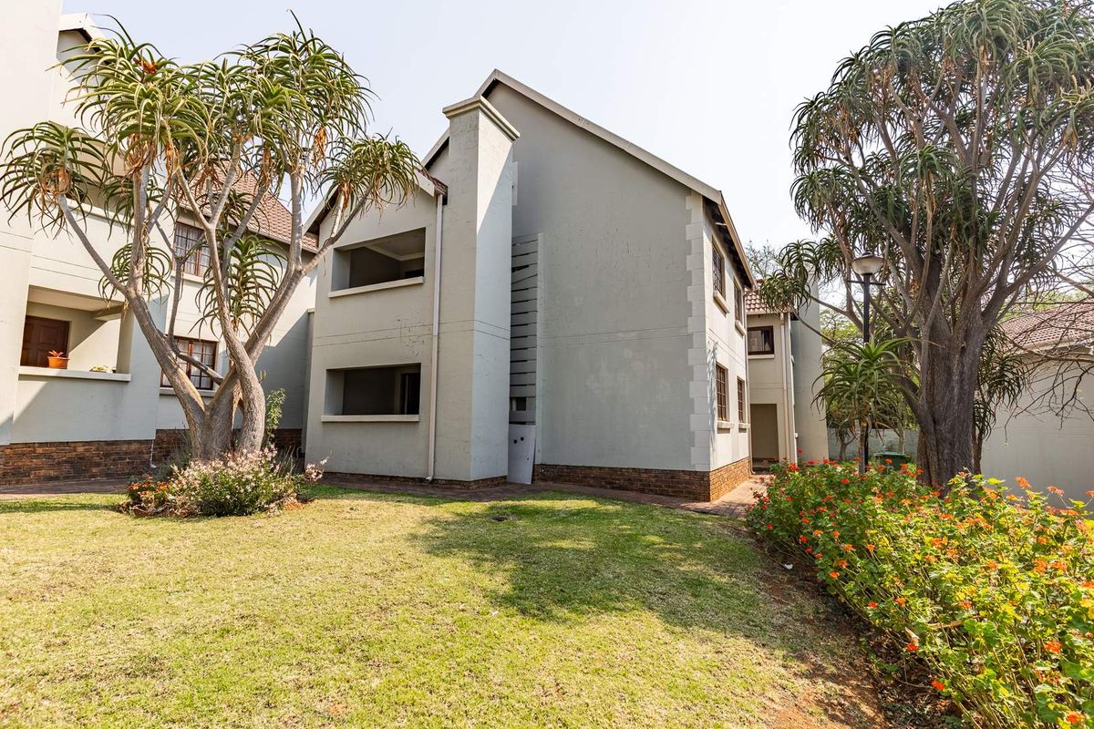 Exterior view of the apartment building featuring a landscaped garden, paved walkways, and private balconies with visible brick plinth detailing.