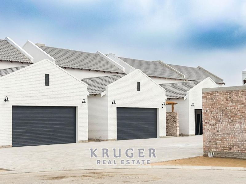 Modern townhouse complex featuring white brick facades, grey tiled roofs, and multiple garage bays with a paved driveway.