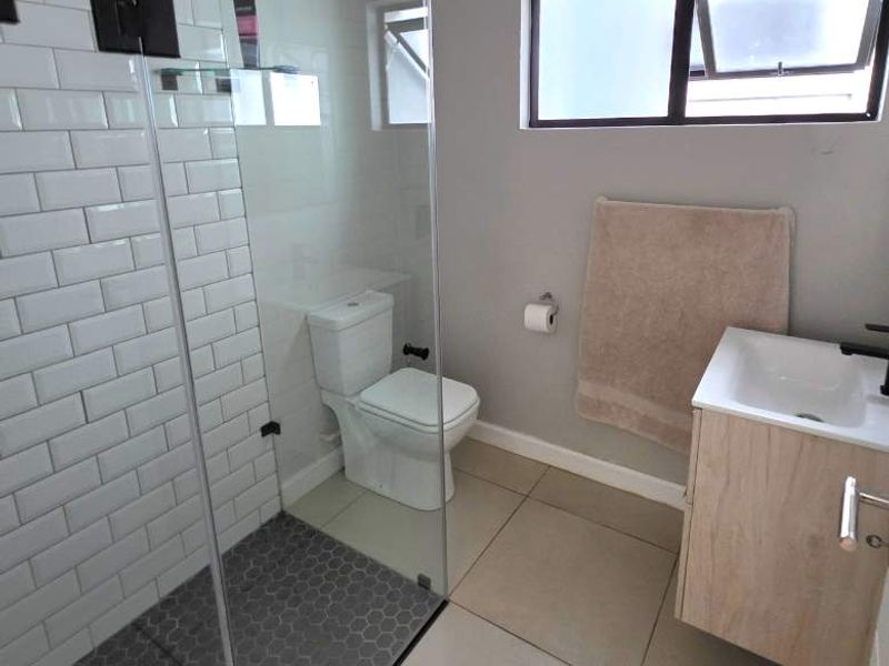 Modern bathroom featuring a glass-enclosed shower with subway tiles, hexagonal floor tiling, and a contemporary wall-mounted vanity unit.
