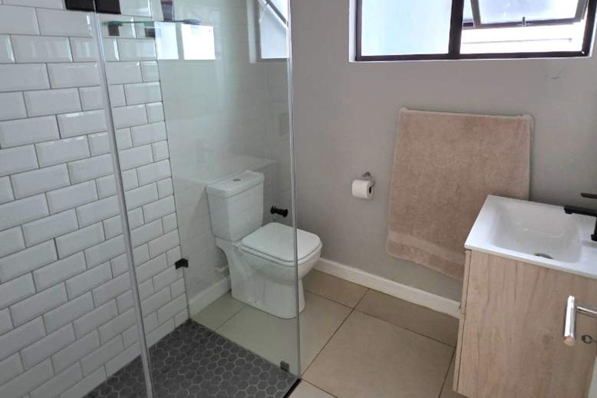 Modern bathroom featuring a glass-enclosed shower with subway tiles, hexagonal floor tiling, and a contemporary wall-mounted vanity unit.