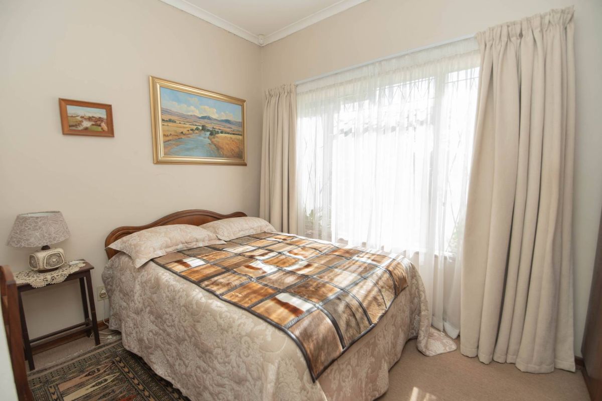 A cozy bedroom featuring neutral wall tones, carpeted flooring, and large windows dressed with curtains, providing a comfortable and well-lit living space.