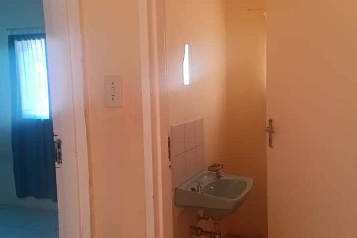 A small bathroom area featuring a wall-mounted basin with tiled splashback, adjacent to a doorway leading into a bedroom.