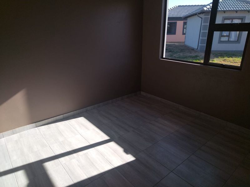 A bright, empty bedroom featuring modern wood-look floor tiles and a large aluminium-framed window.