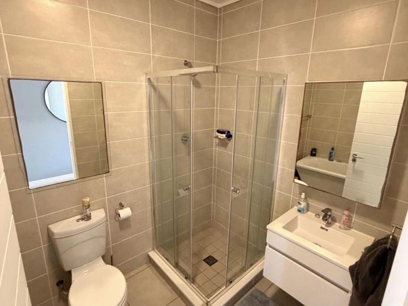 A modern, well-maintained bathroom featuring a glass shower enclosure, wall-mounted vanity, and neutral ceramic tiling throughout.