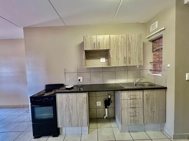 A functional kitchen featuring light wood-look cabinetry, granite countertops, a stainless steel sink, and a built-in stove with tiled flooring.