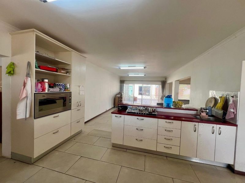 Open-plan kitchen featuring built-in cabinetry, gas hob, and tiled flooring, flowing into a spacious living area with access to the rear exterior.