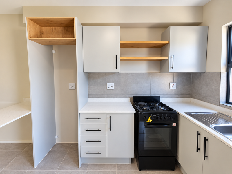 Modern kitchen featuring light grey cabinetry, stone countertops, open shelving, tiled backsplash, and a freestanding gas stove with oven.