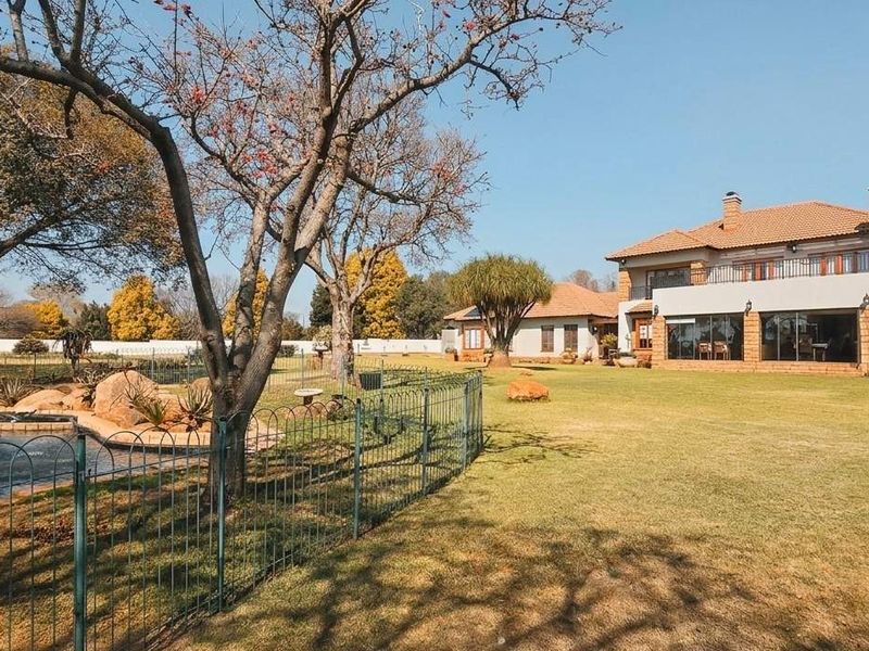 Spacious rear exterior view of the house featuring a large landscaped garden, a swimming pool with safety fencing, and a multi-level brick facade.