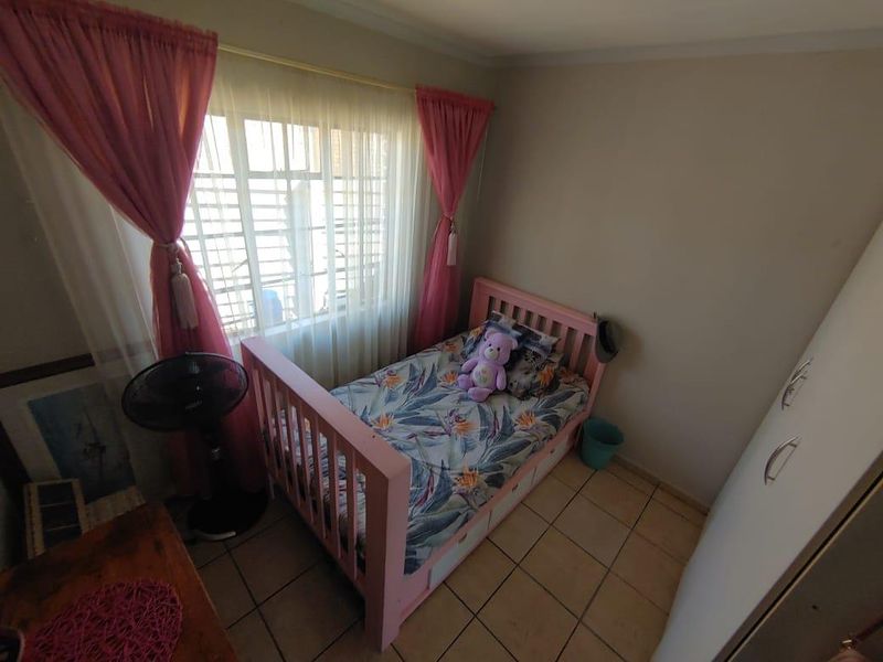 A functional bedroom featuring tiled flooring, a built-in wardrobe, and a window fitted with security burglar bars.