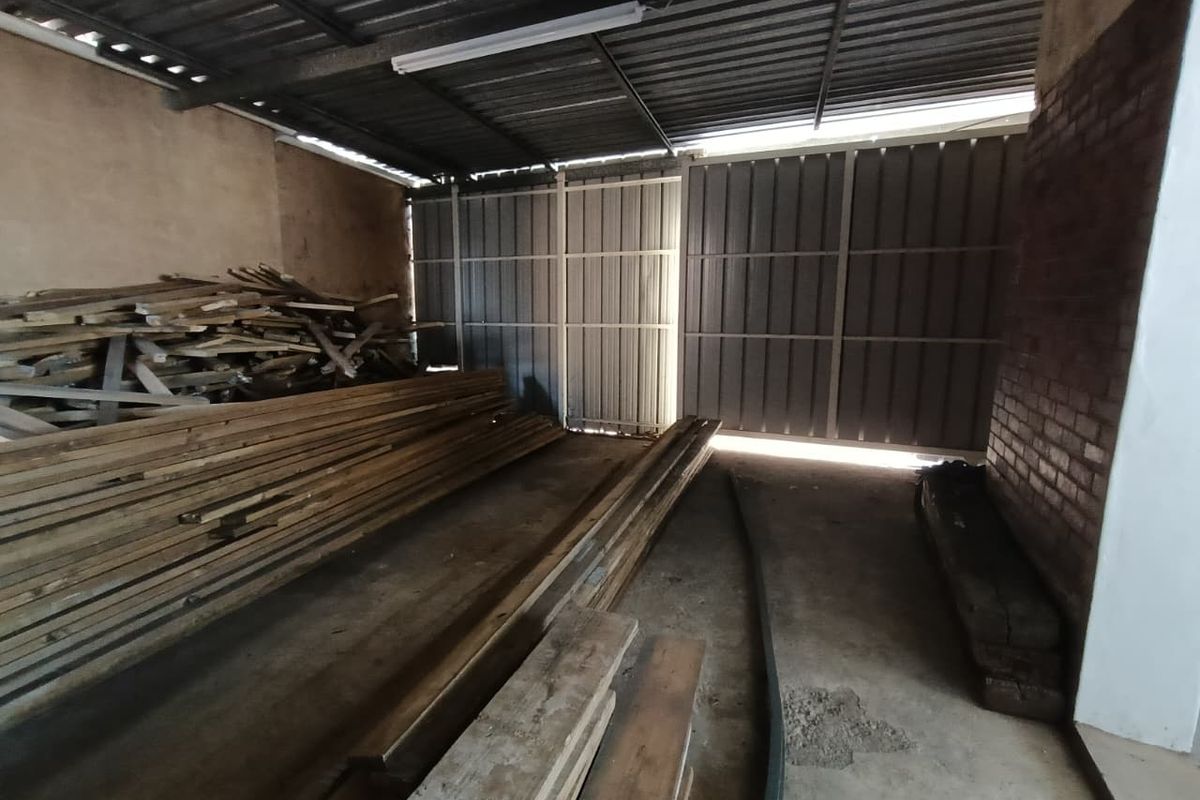 A spacious industrial garage or storage area featuring concrete flooring, exposed brickwork, and large metal sliding doors.