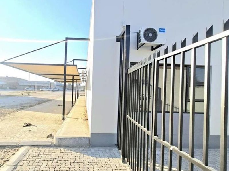 Exterior view of the office building featuring a paved driveway, metal security fencing, and a covered walkway canopy.