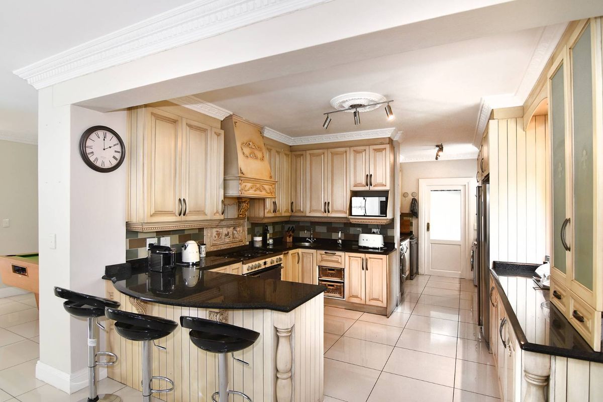 A traditional kitchen featuring light-toned cabinetry, dark granite countertops, a breakfast bar, and tiled flooring with integrated appliances.